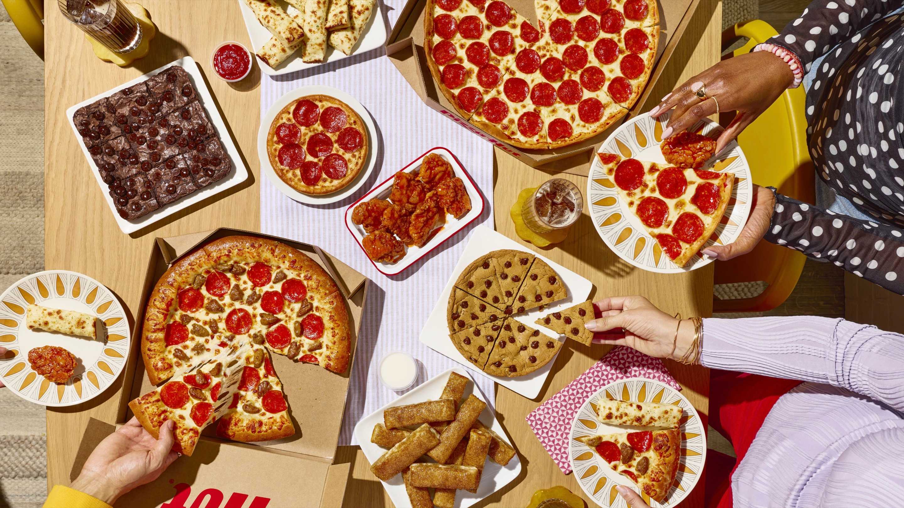 Mesa con pizzas, alitas, palitos de pan y postres de Pizza Hut